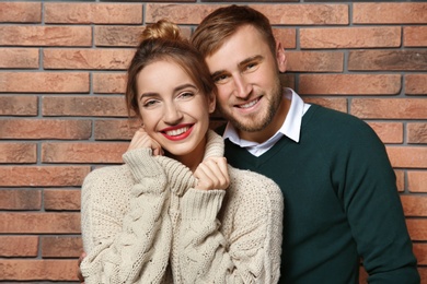 Young couple in warm sweaters near brick wall