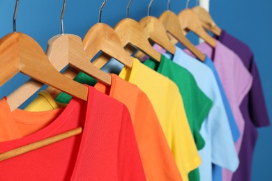 Photo of Bright clothes on wooden hangers against blue background, closeup. Rainbow colors