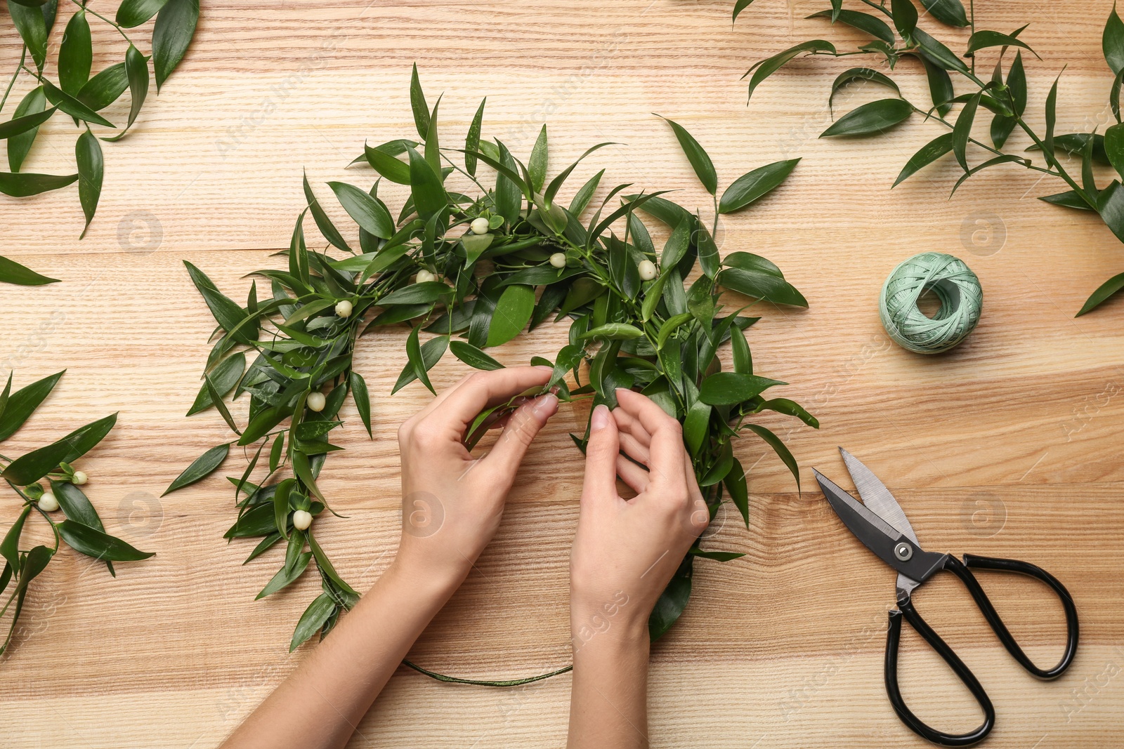 Photo of Florist making beautiful mistletoe wreath at wooden table, top view. Traditional Christmas decor