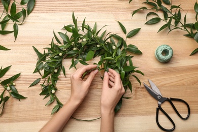 Photo of Florist making beautiful mistletoe wreath at wooden table, top view. Traditional Christmas decor