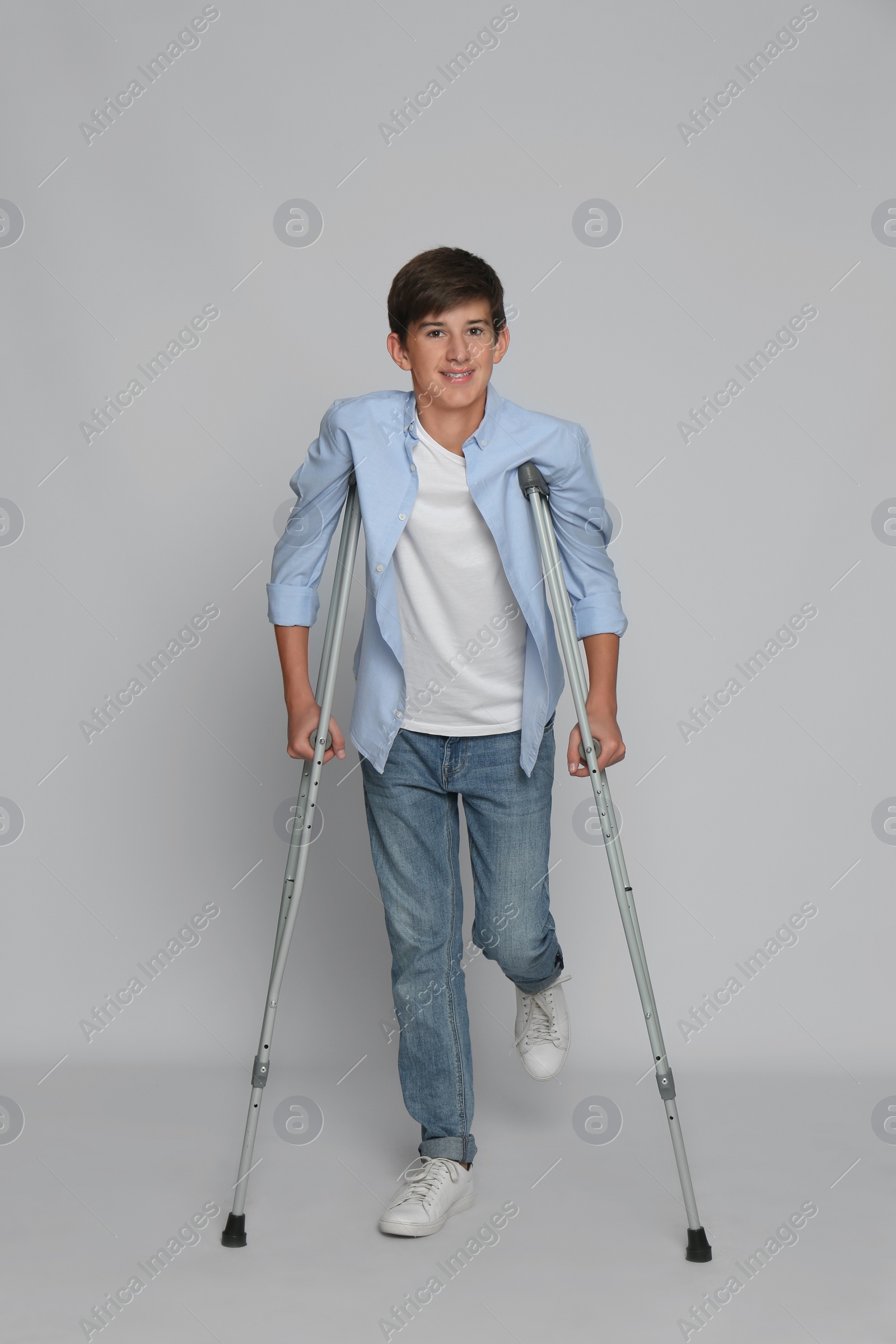 Photo of Teenage boy with injured leg using crutches on grey background