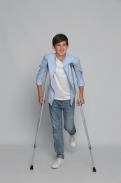 Photo of Teenage boy with injured leg using crutches on grey background