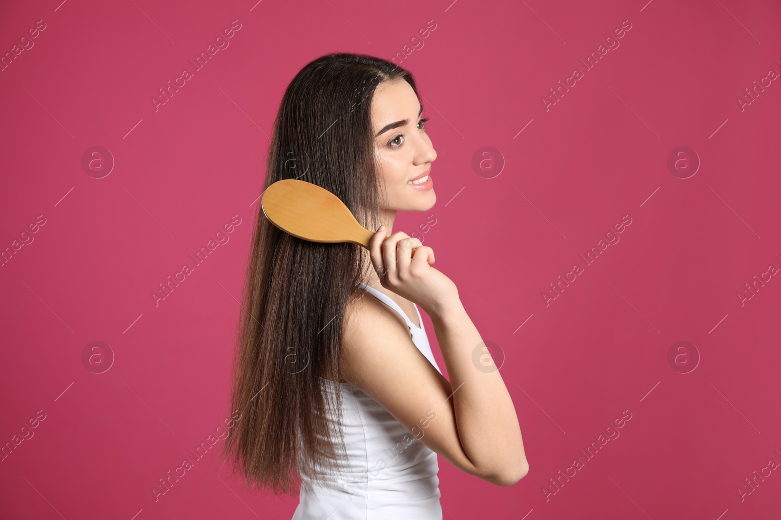 Photo of Beautiful smiling young woman with hair brush on color background