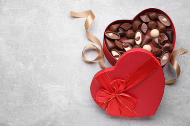 Heart shaped box with delicious chocolate candies and ribbon on light grey table, flat lay. Space for text