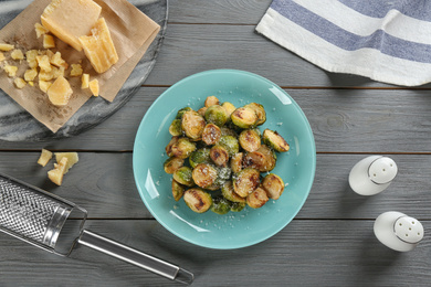 Photo of Delicious roasted brussels sprouts with grated cheese served on grey wooden table, flat lay