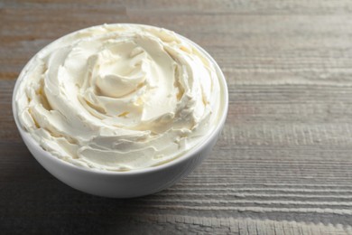 Photo of Bowl of tasty cream cheese on wooden table, space for text