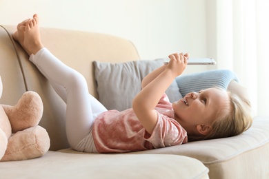 Cute little girl with smartphone on sofa in room