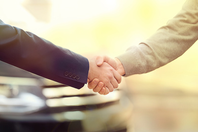 Image of Salesman shaking hands with customer in modern auto dealership, closeup. Buying new car