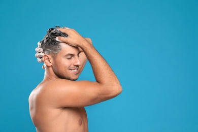 Photo of Handsome man washing hair on light blue background, space for text