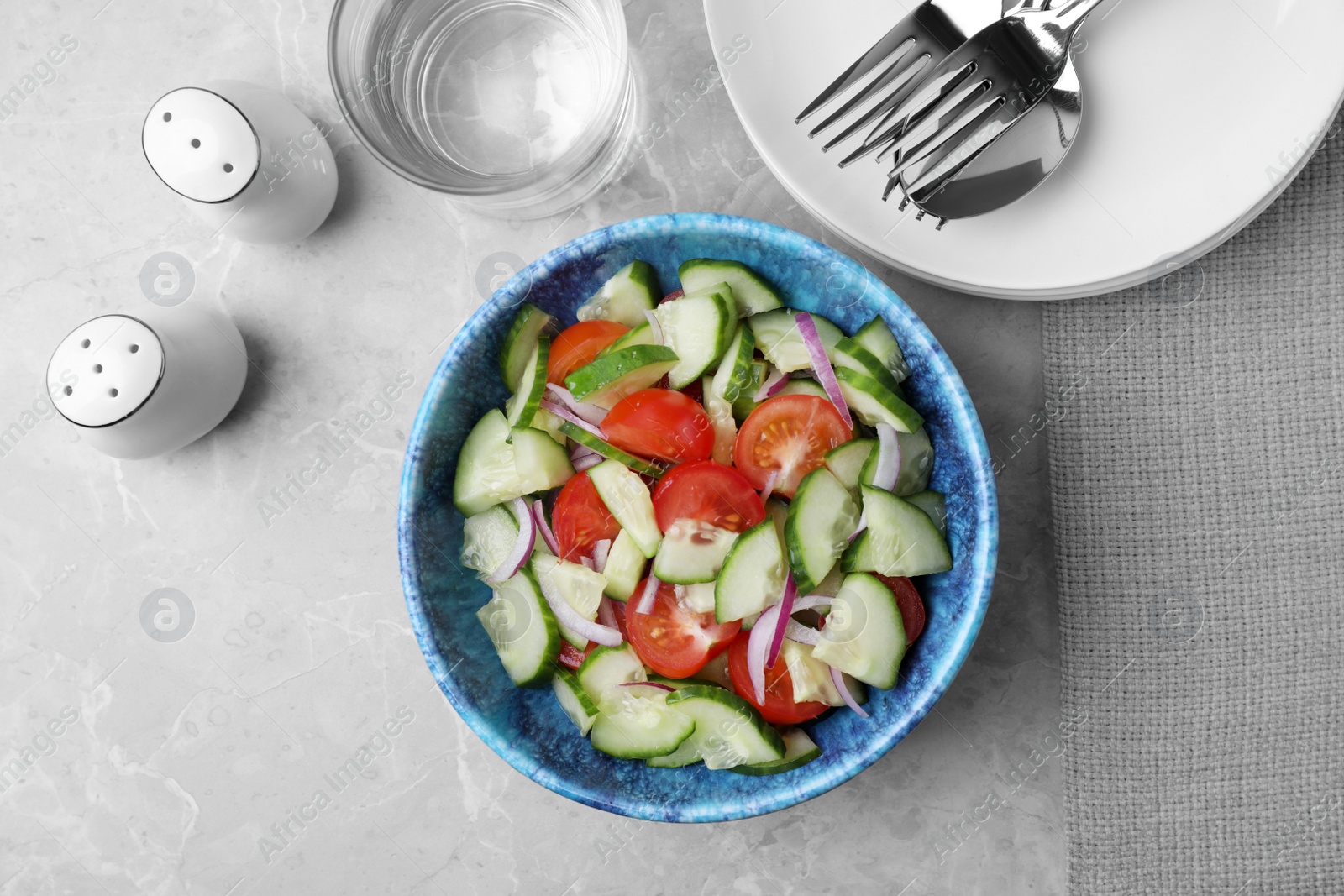 Photo of Bowl of vegetarian salad with cucumber, tomato and onion served on table, flat lay