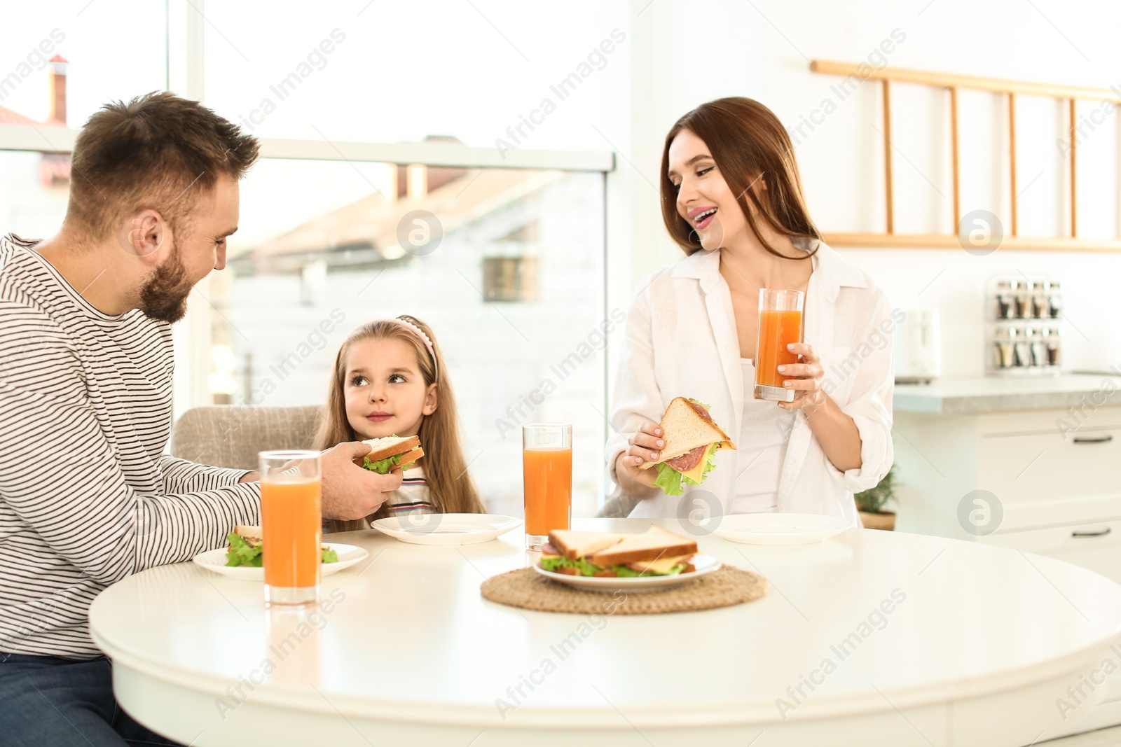 Photo of Happy family having breakfast with sandwiches at table in kitchen