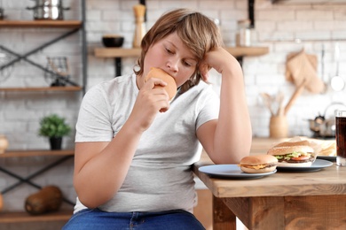 Overweight boy at table with fast food in kitchen