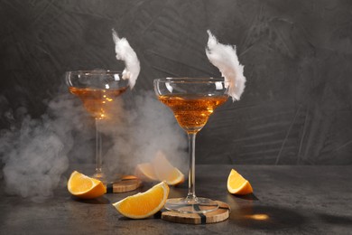 Tasty cocktails in glasses decorated with cotton candy and orange slices on gray table