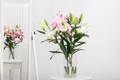 Photo of Vase with bouquet of beautiful lilies on white table near mirror