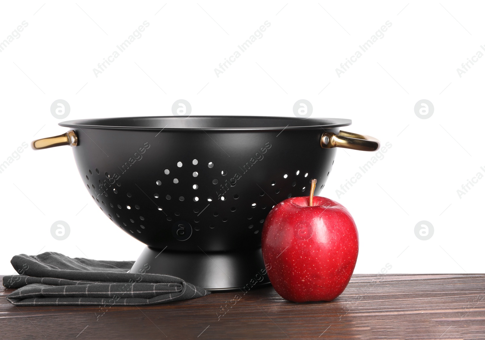 Photo of Black colander, apple and napkin on wooden table against white background