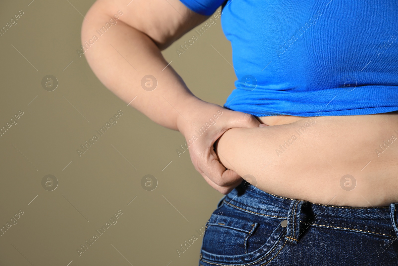 Photo of Overweight woman in tight shirt and jeans on light brown background, closeup