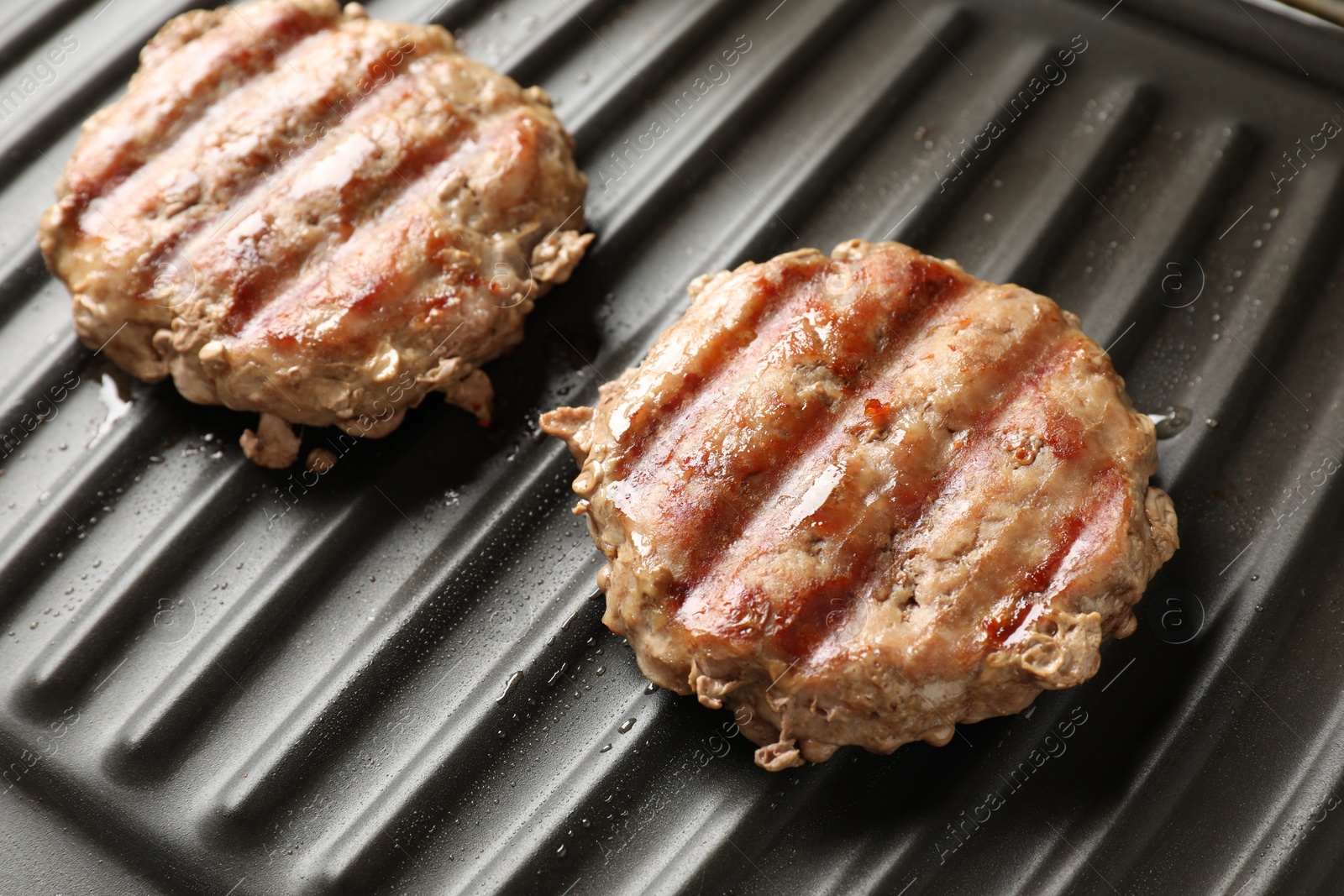 Photo of Delicious hamburger patties cooking on electric grill, closeup