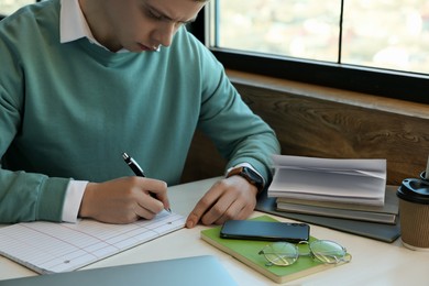 Photo of Young male student with books studying at table in cafe, closeup