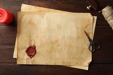 Sheet of old parchment paper with wax stamp, rope, scissors and candle on wooden table, flat lay