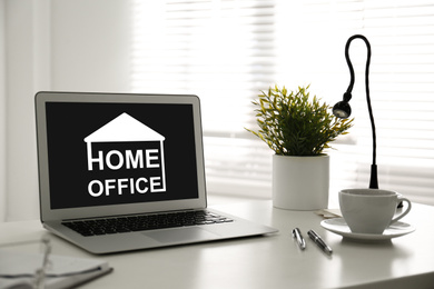 Modern laptop with text HOME OFFICE on white table indoors