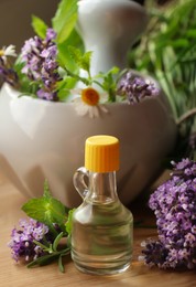 Bottle of natural lavender essential oil near mortar with flowers on wooden table