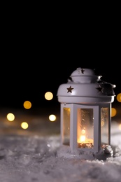 Lantern with burning candle and Christmas lights on white snow outdoors