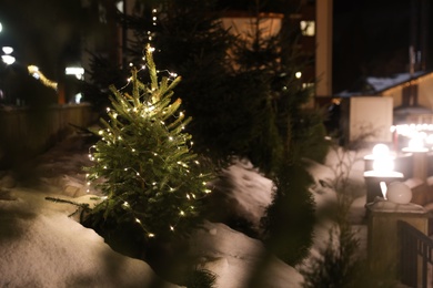 Photo of Beautiful conifer tree with glowing Christmas lights on street, space for text. Winter holiday
