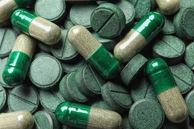 Photo of Green spirulina pills and capsules as background, closeup