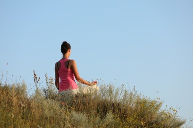Photo of Woman meditating in meadow, back view. Space for text