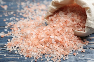 Photo of Overturned bag with pink himalayan salt on blue wooden table, closeup