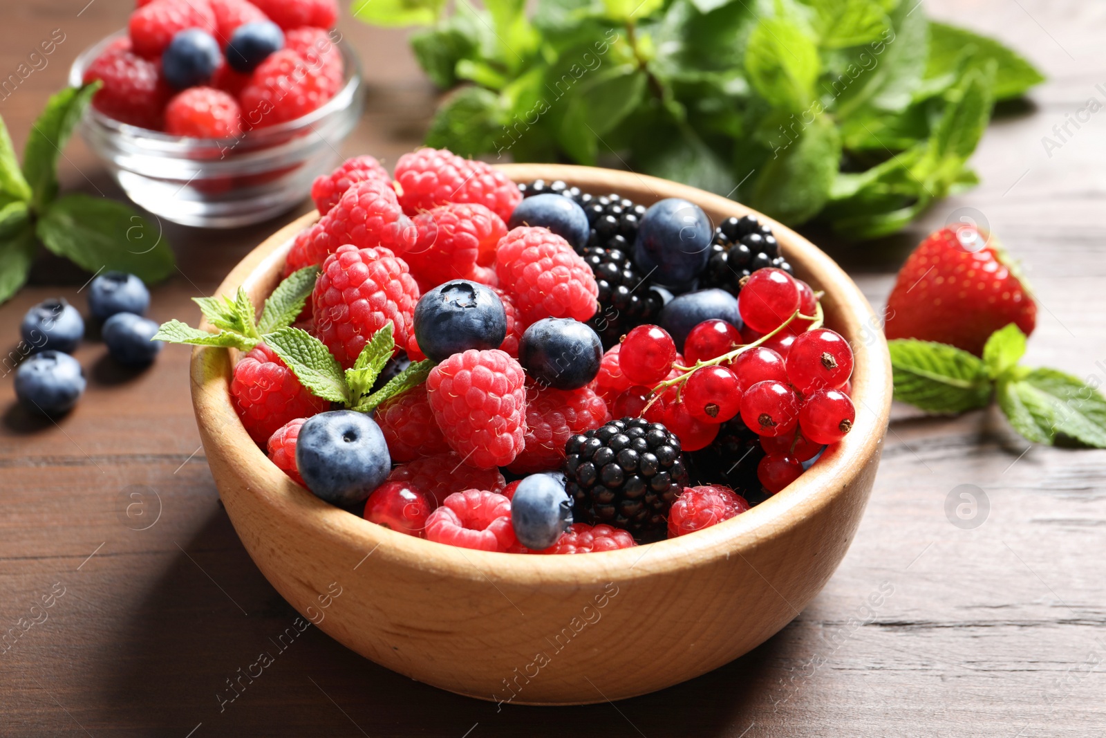 Photo of Bowl with raspberries and different berries on wooden table