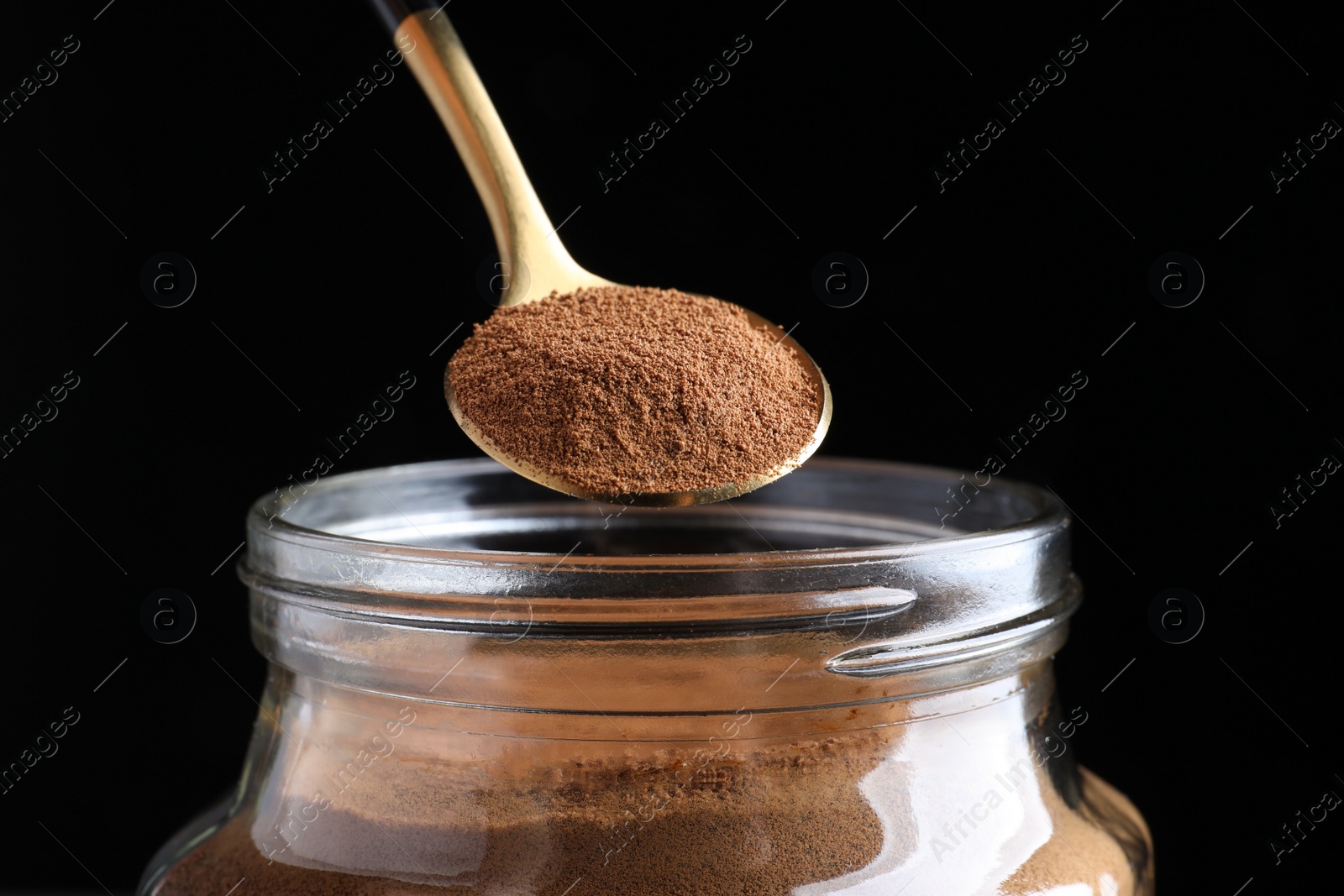 Photo of Spoon of instant coffee over jar against black background, closeup