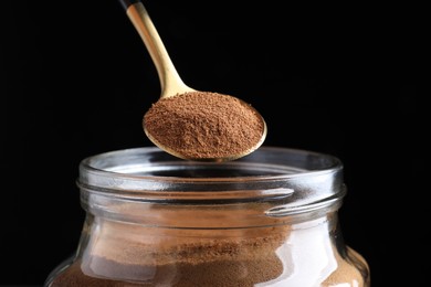 Spoon of instant coffee over jar against black background, closeup