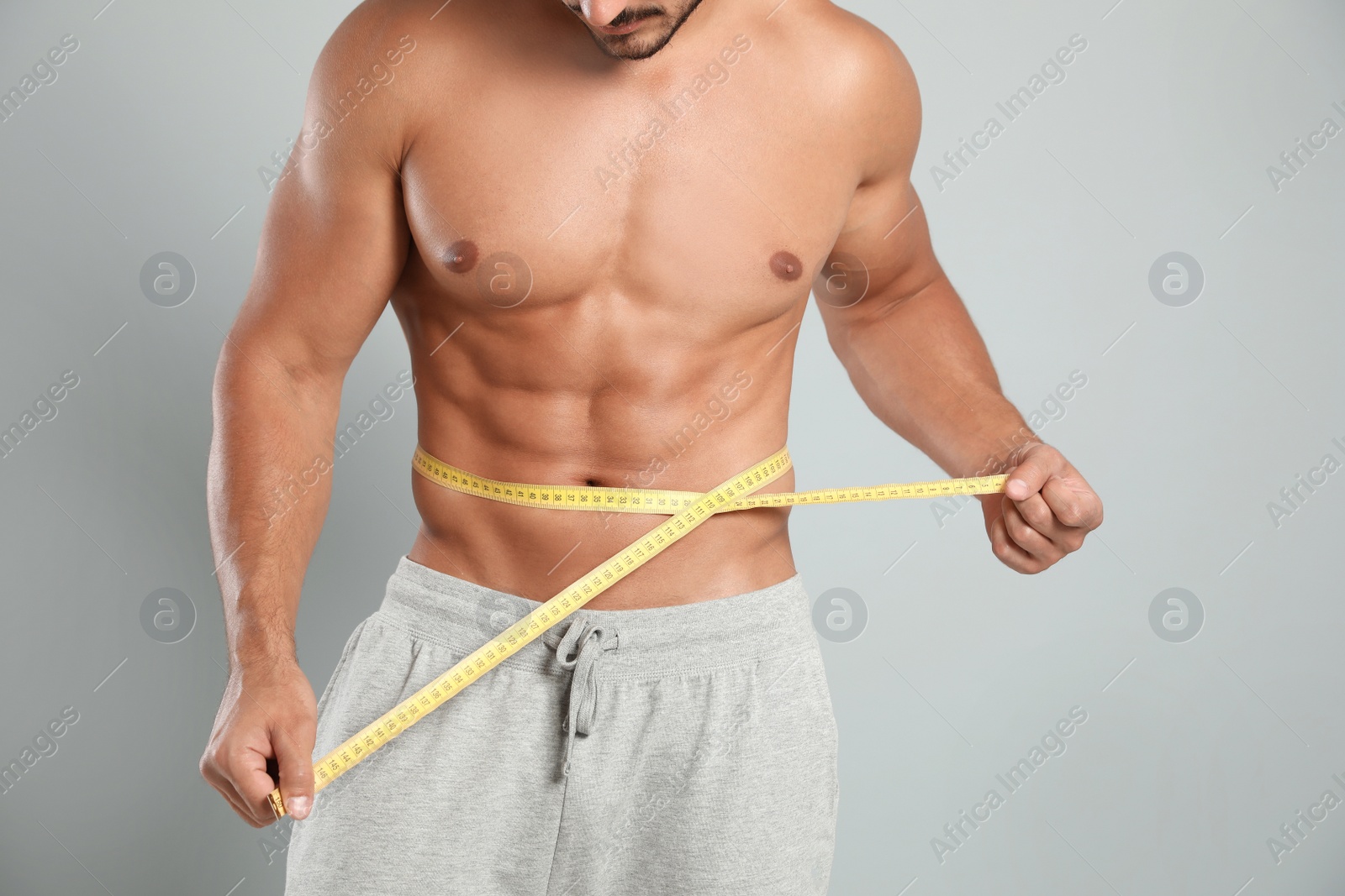 Photo of Young man with slim body using measuring tape on grey background, closeup view