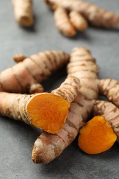 Photo of Whole and cut turmeric roots on grey table, closeup