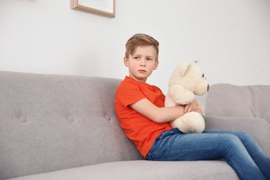 Photo of Little autistic boy sitting on sofa with toy at home