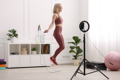 Photo of Smiling sports blogger jumping with rope while streaming online fitness lesson at home