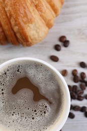 Coffee to go. Paper cup with tasty drink, croissant and beans on white wooden table, flat lay