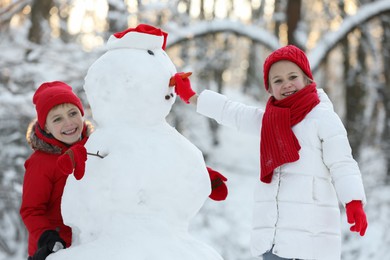 Photo of Cute little girl and boy making snowman in winter park