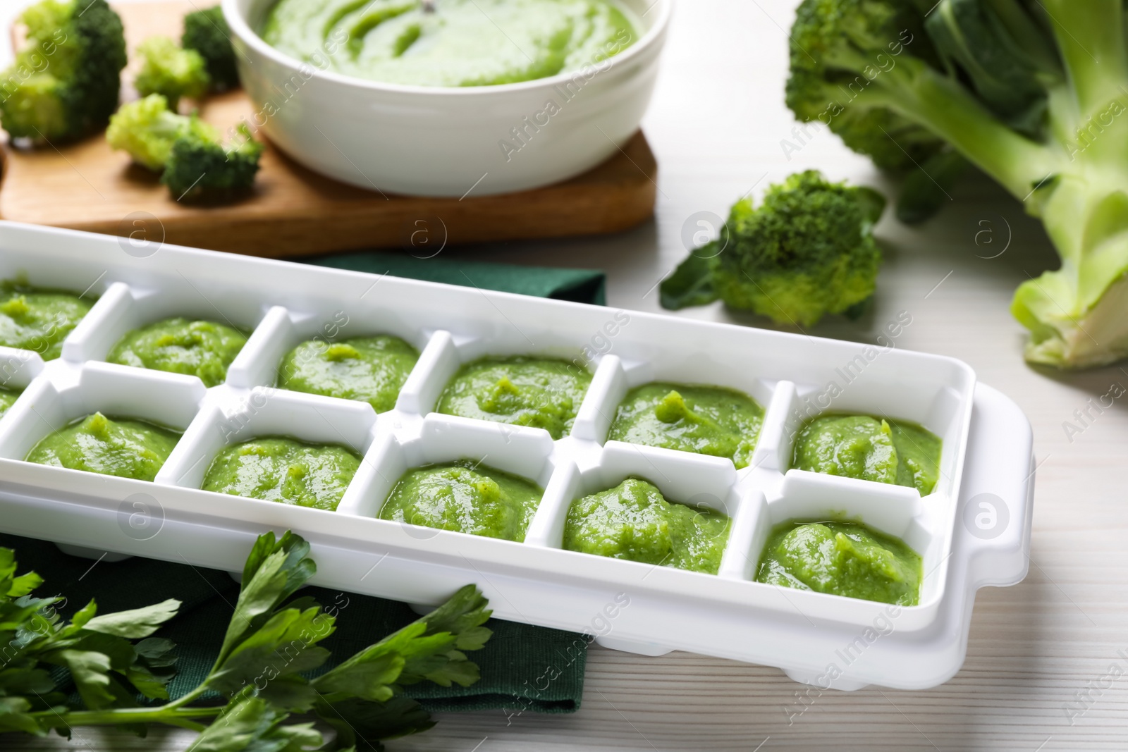 Photo of Broccoli puree in ice cube tray and ingredients on white wooden table. Ready for freezing