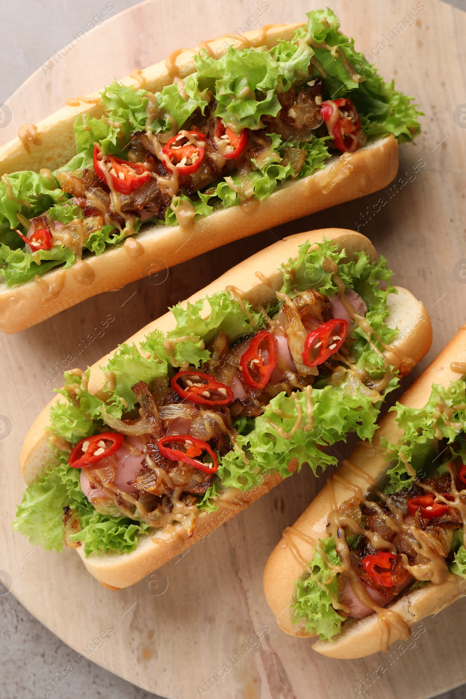 Photo of Tasty hot dogs with chili, lettuce and sauce on grey textured table, top view