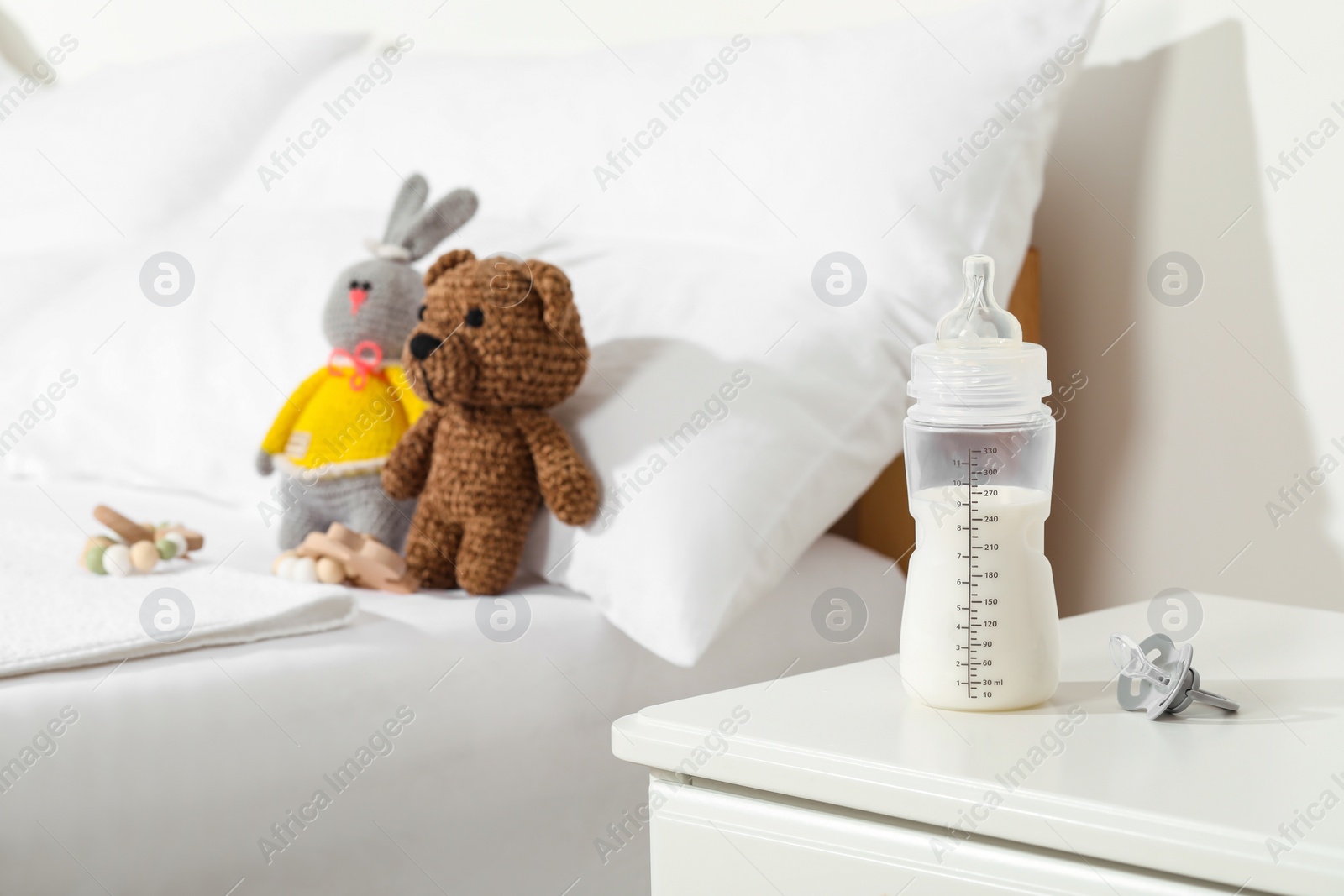 Photo of Feeding bottle with milk on nightstand near baby bed indoors. Space for text