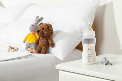 Feeding bottle with milk on nightstand near baby bed indoors. Space for text