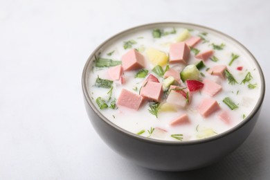 Delicious cold summer soup (okroshka) with boiled sausage in bowl on white table, space for text