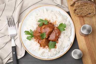 Photo of Delicious goulash served with rice on grey wooden table, flat lay