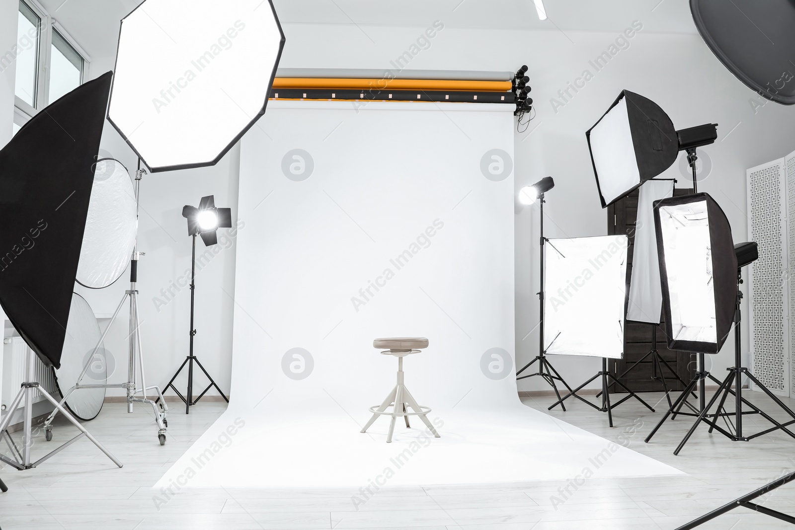 Photo of Tripod with camera, bar stool and professional lighting equipment in modern photo studio