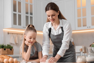 Photo of Making bread. Mother and her daughter kneading dough at wooden table in kitchen