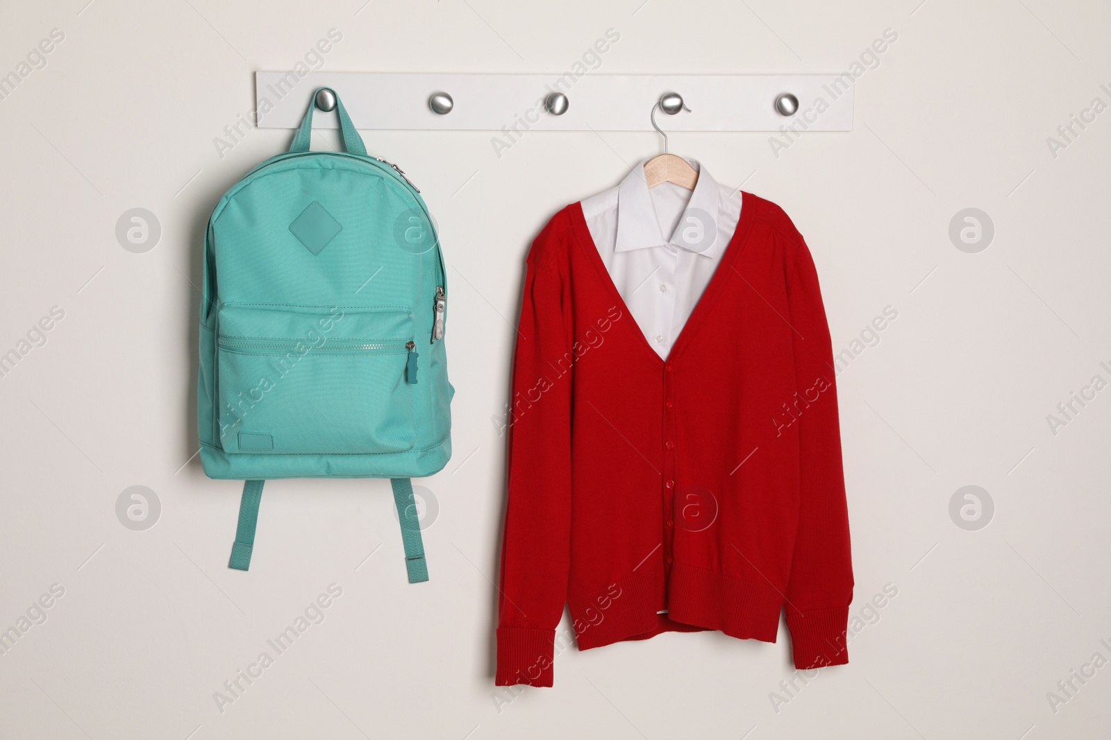 Photo of Shirt, jumper and bag hanging on white wall. School uniform
