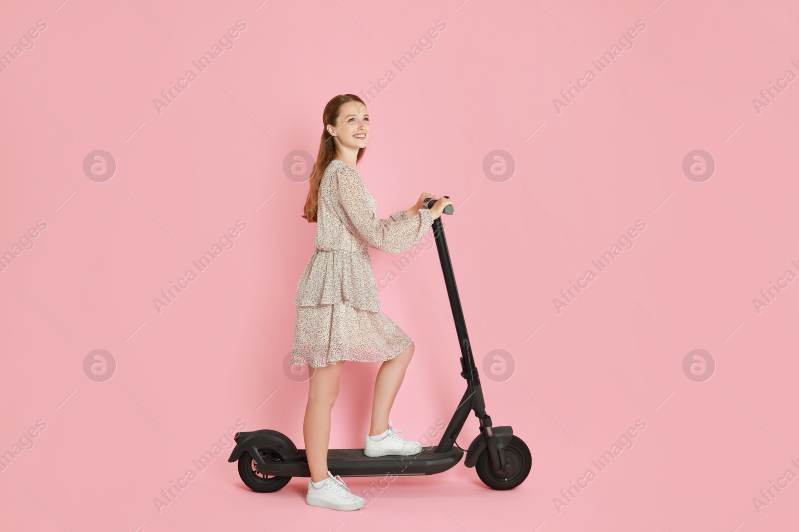 Photo of Happy woman with modern electric kick scooter on pink background