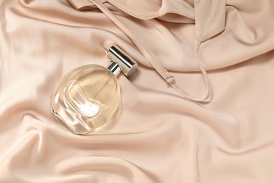 Photo of Luxury perfume in bottle on beige silk fabric, top view